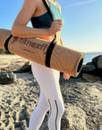 Tappetino Fitnexfly in sughero e gomma naturali arrotolato trasportato sul braccio da ragazza in outfit sportivo
