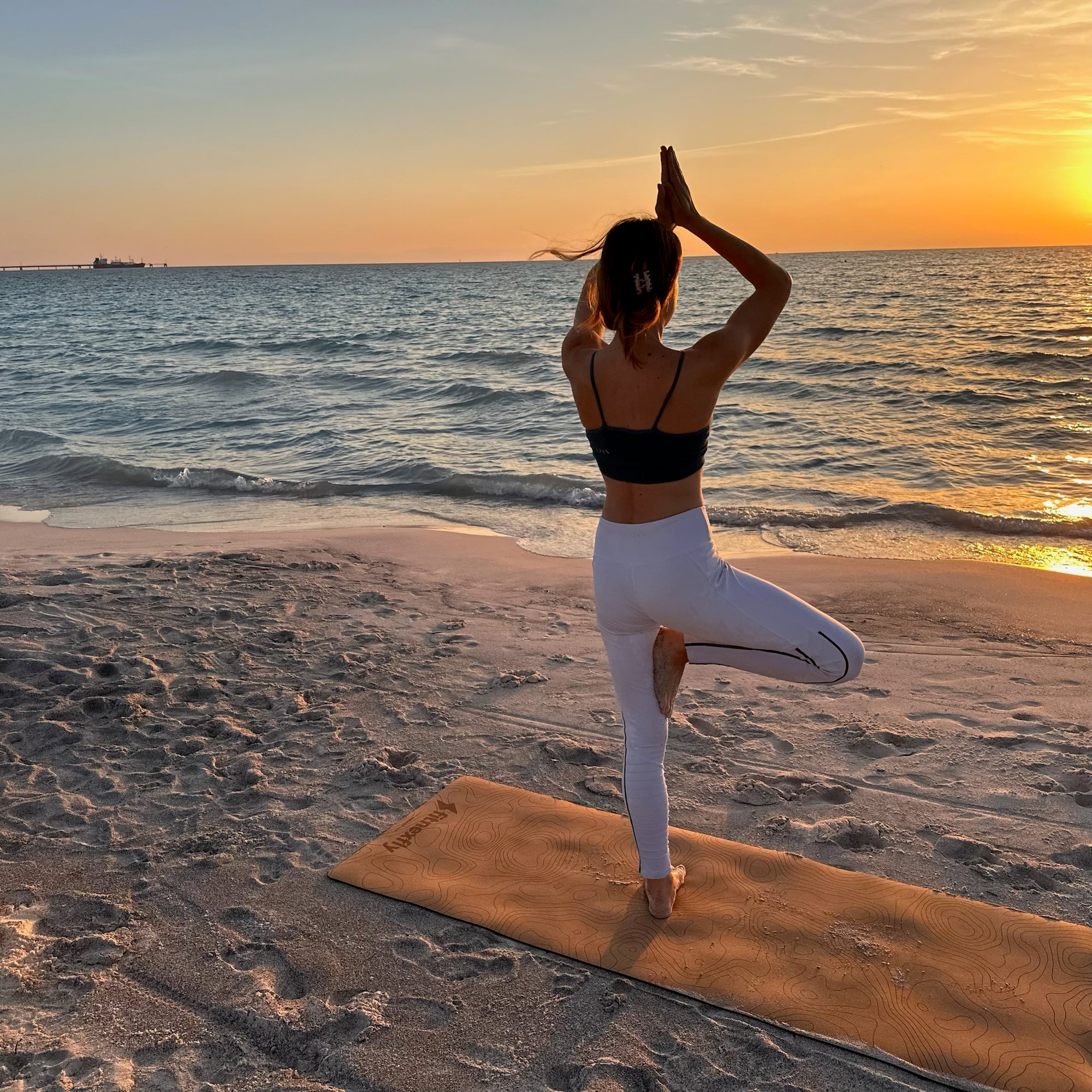 Fitnexfly donna in equilibrio su una gamba con l'altra a 90 gradi  vista di schiena che saluta il sole al tramonto