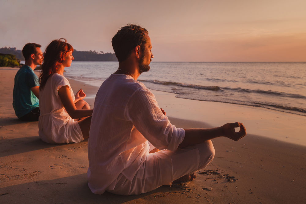 tre persone in riva al mare fanno yoga al tramonto